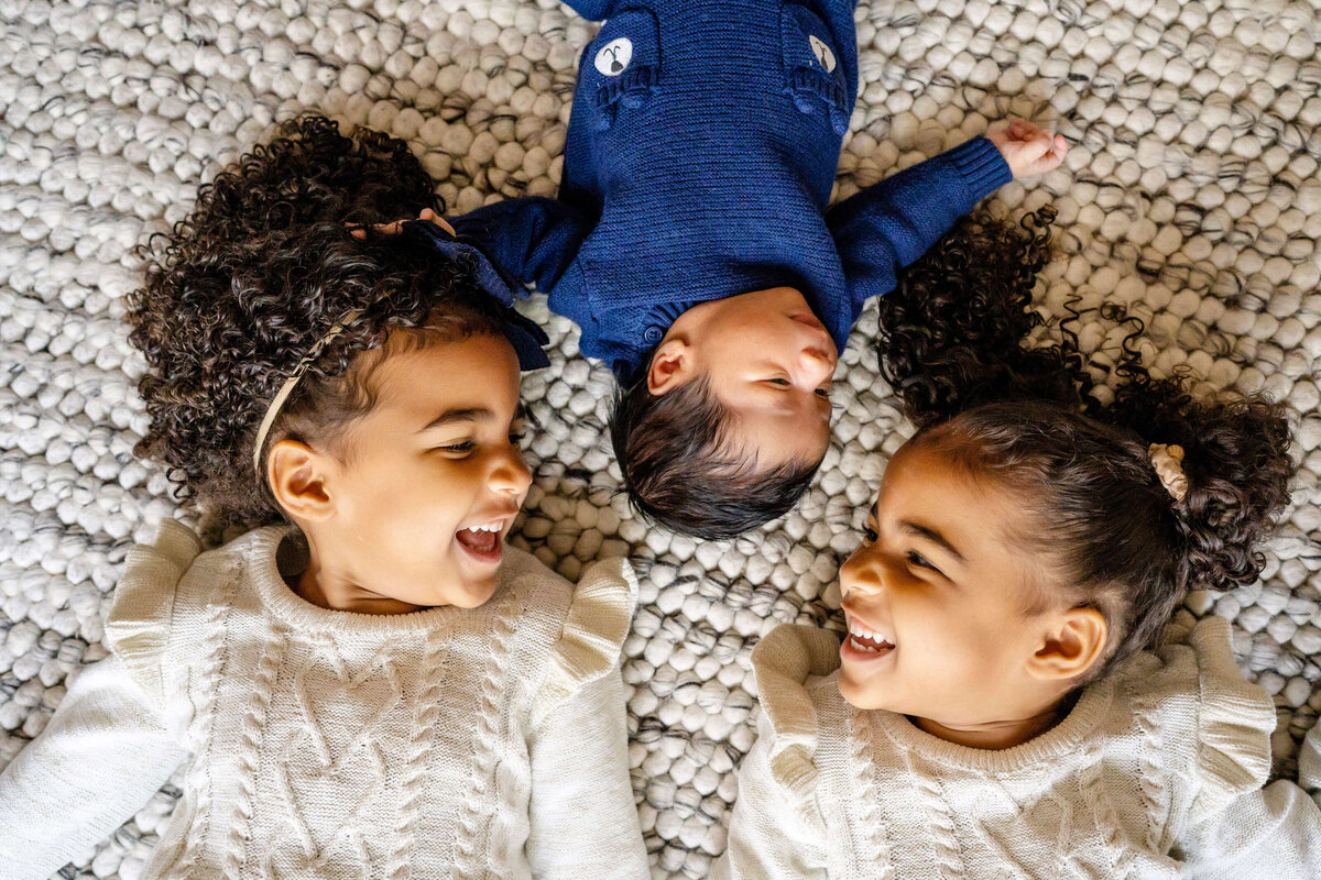 Twin girls laying on floor smiling at newborn brother