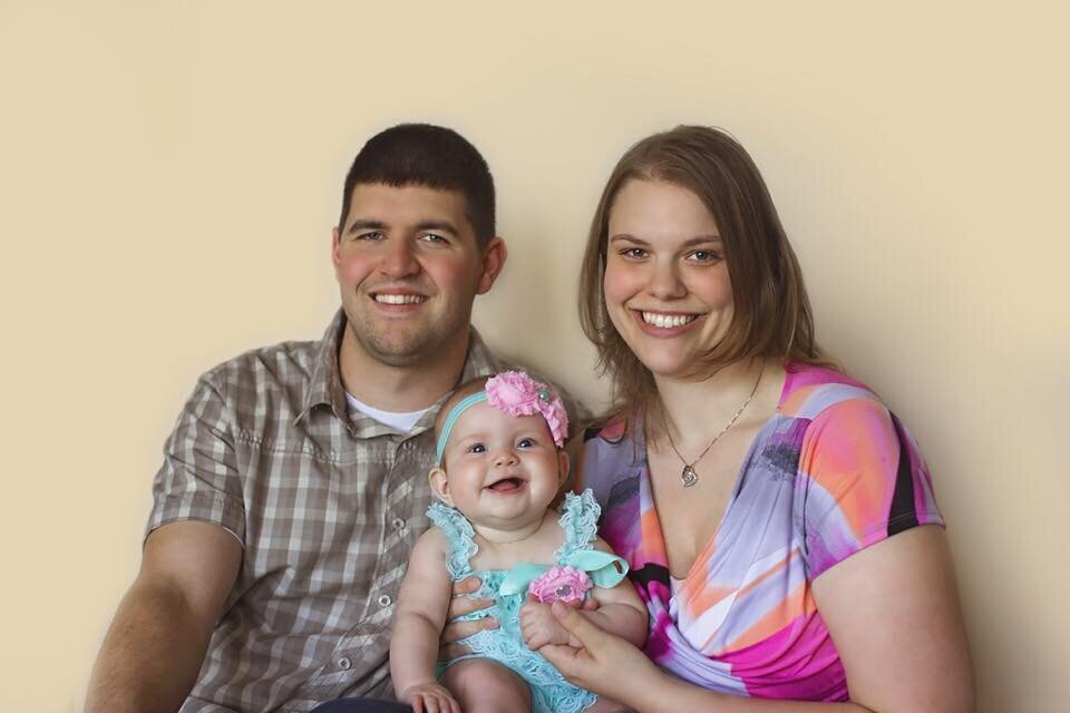 A picture of me with my husband and our daughter at 9 months old in a photographer's studio.