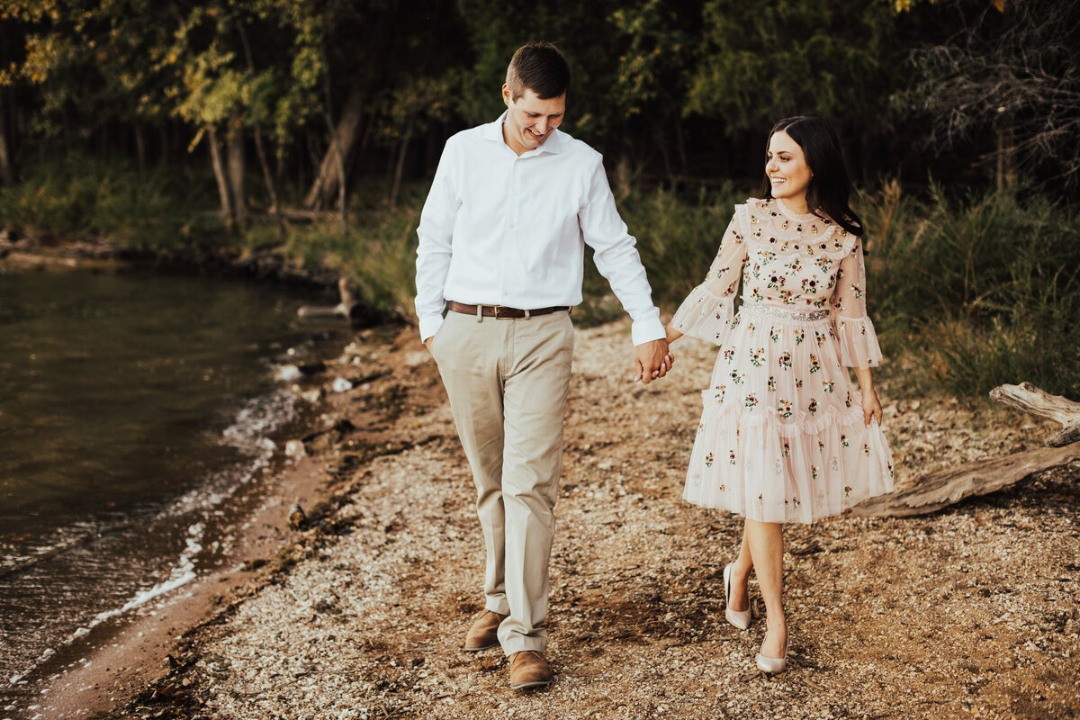 couple holding hands walking next to water