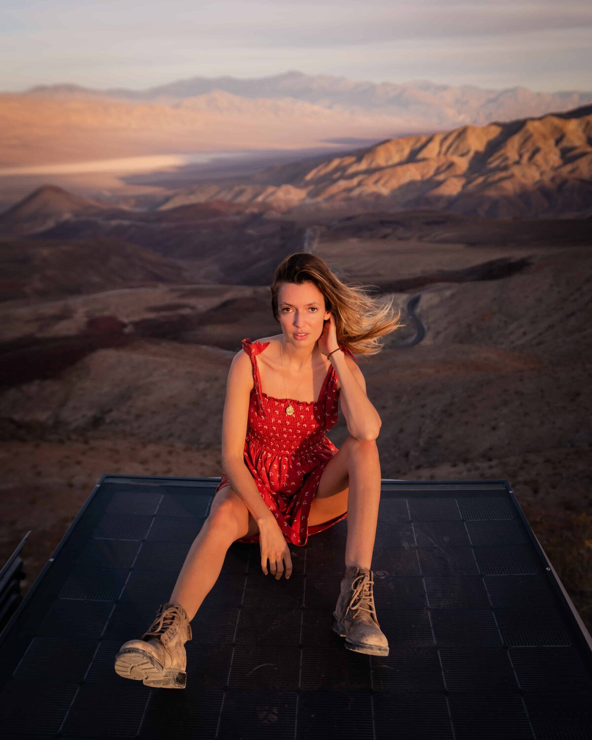 Woman in a red dress sitting on the ground with mountains in the background