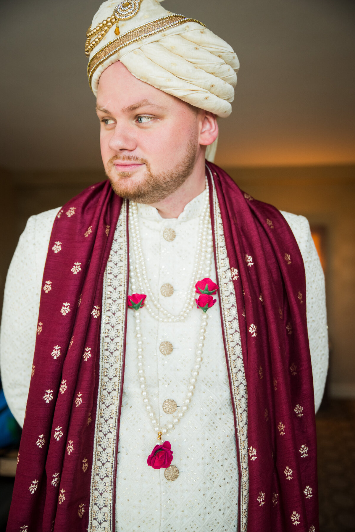 A groom looks off camera, dressed in the traditional Indian wedding attire.