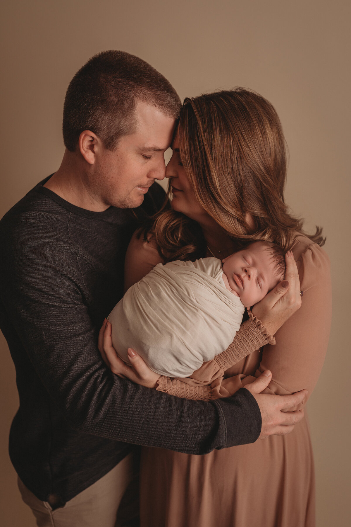 Photography session at Woodstock GA newborn photography studio of mom, dad and baby snuggling close closing eyes.