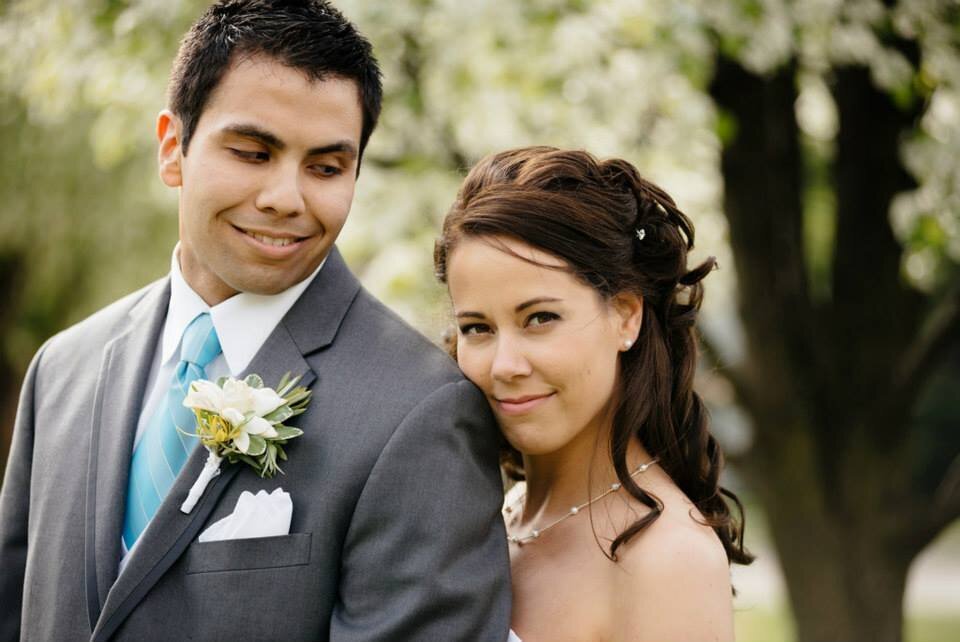A couple share a tender moment outside before entering the reception. Spring flowers are on the trees in the background.
