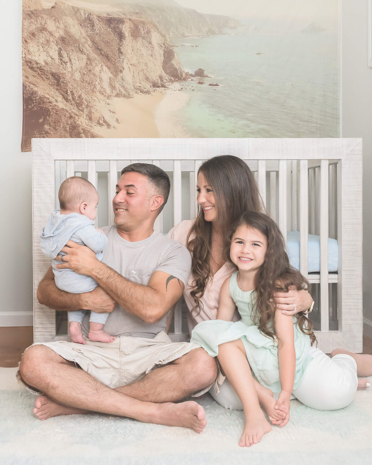 Family photo in serene nursery with lots of  light aqua and light blue with hints of tan, family wearing pastels