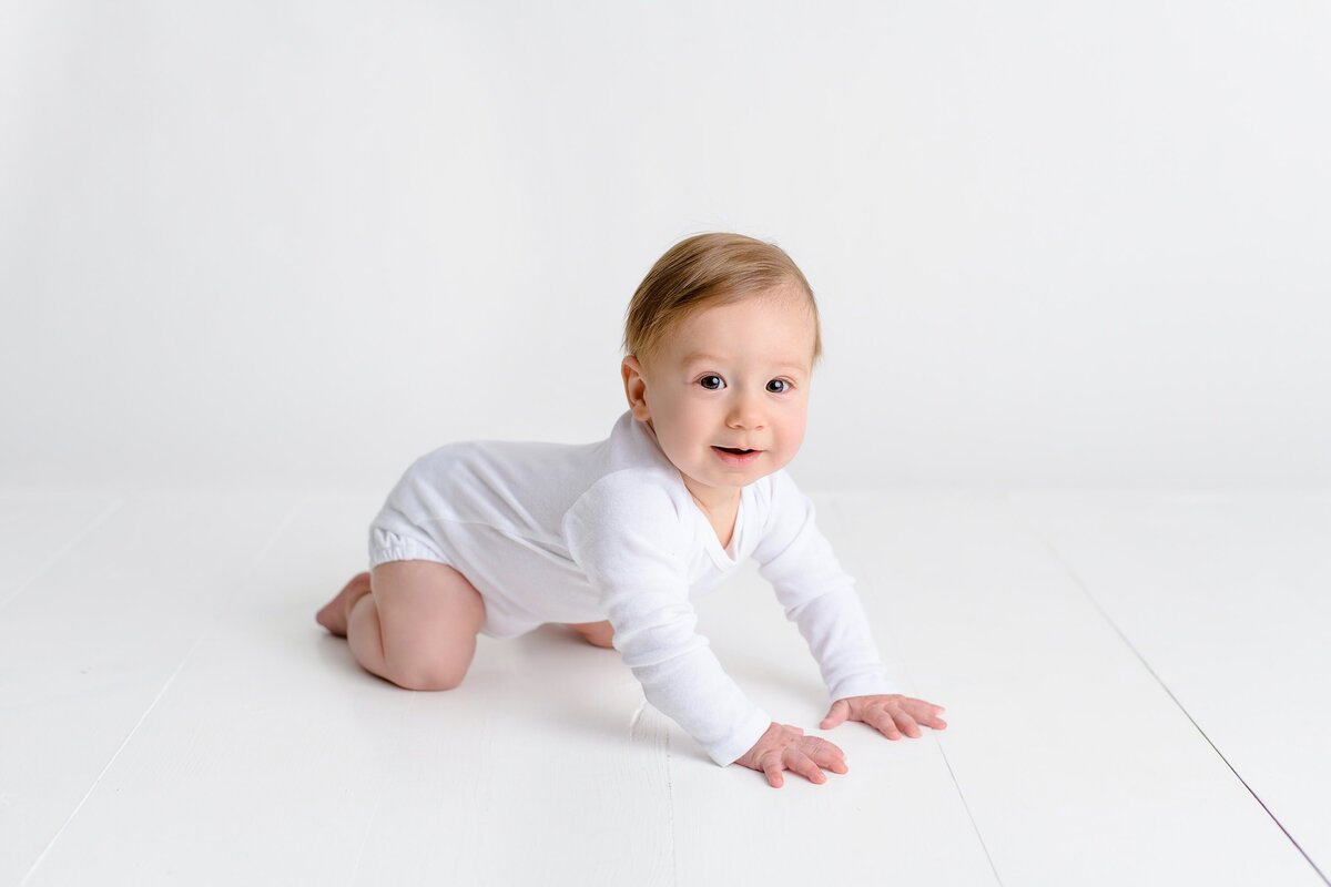 seven month old sitter session with boy dressed in long sleeve white bodysuit in the crawling position.