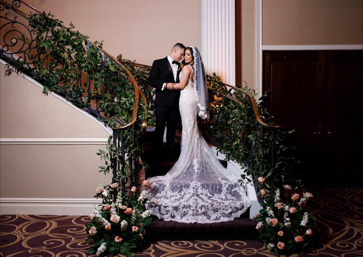 Bride and groom posing in the stairs of an elegant mansion on their wedding day.