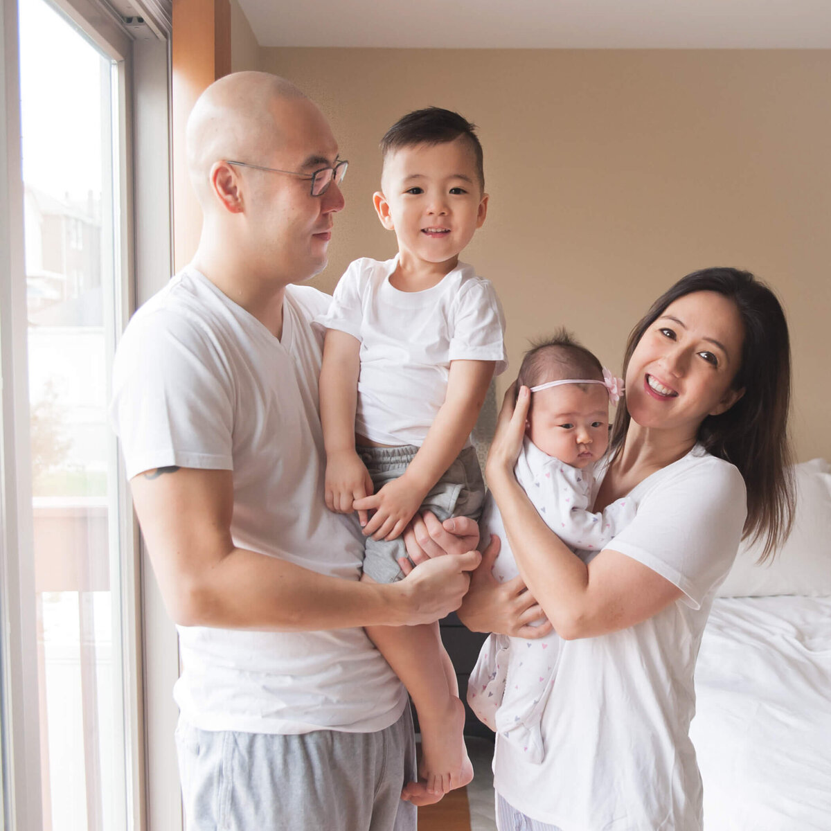 happy family in white and light grey together casually in master bedroom with tan walls