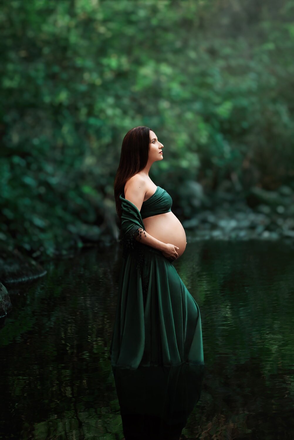 Mom-to-be in emerald green Chicaboo chiffon Chloe skirt standing in a lake and holding her pregnant belly