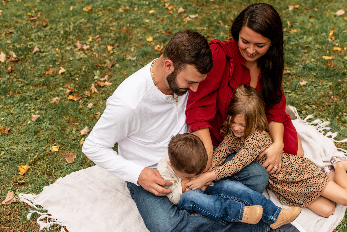 Family tickling each other on blanket in grass