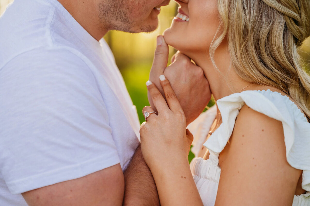 photo of close-up of engagement ring with couple kissing