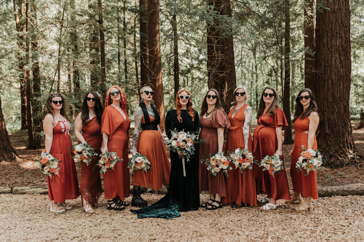 Bride in forest green wedding dress with bridesmaids in orange dresses in the Redwoods at her relaxed forest wedding at Two Woods Estate