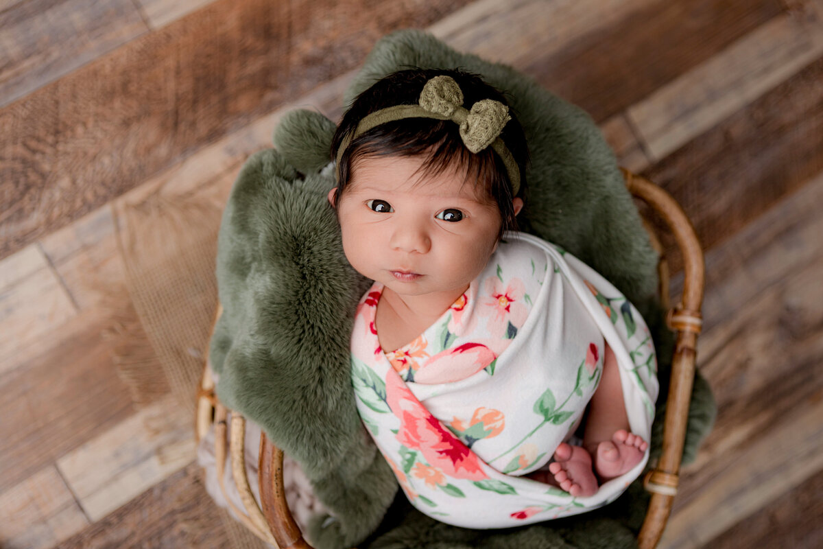 Floral wrapped newborn on an olive green fur in a bamboo basket