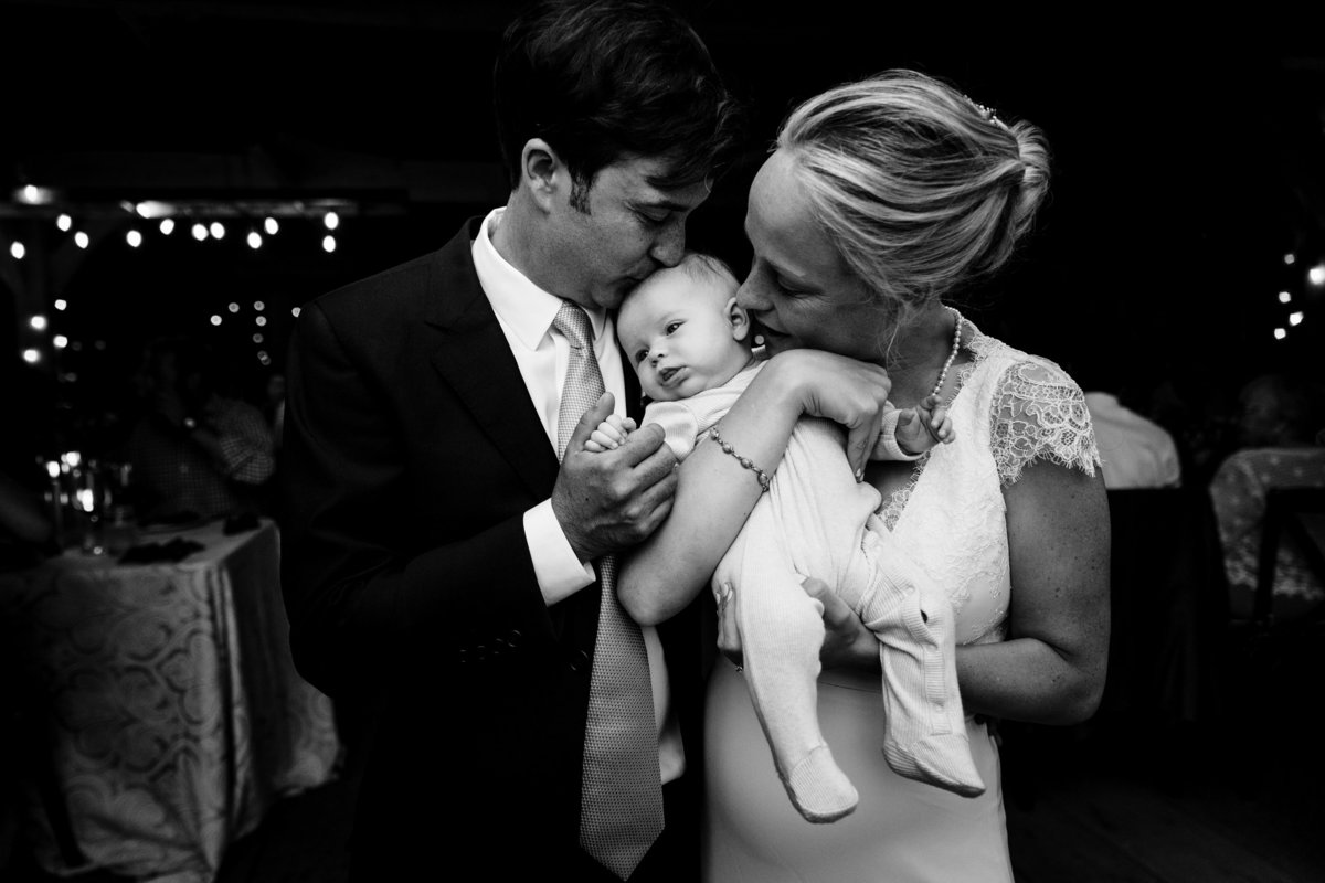 Primo Restaurant Wedding in Rockland Maine the couple kisses their newborn daughter in the barn after their intimate celebration