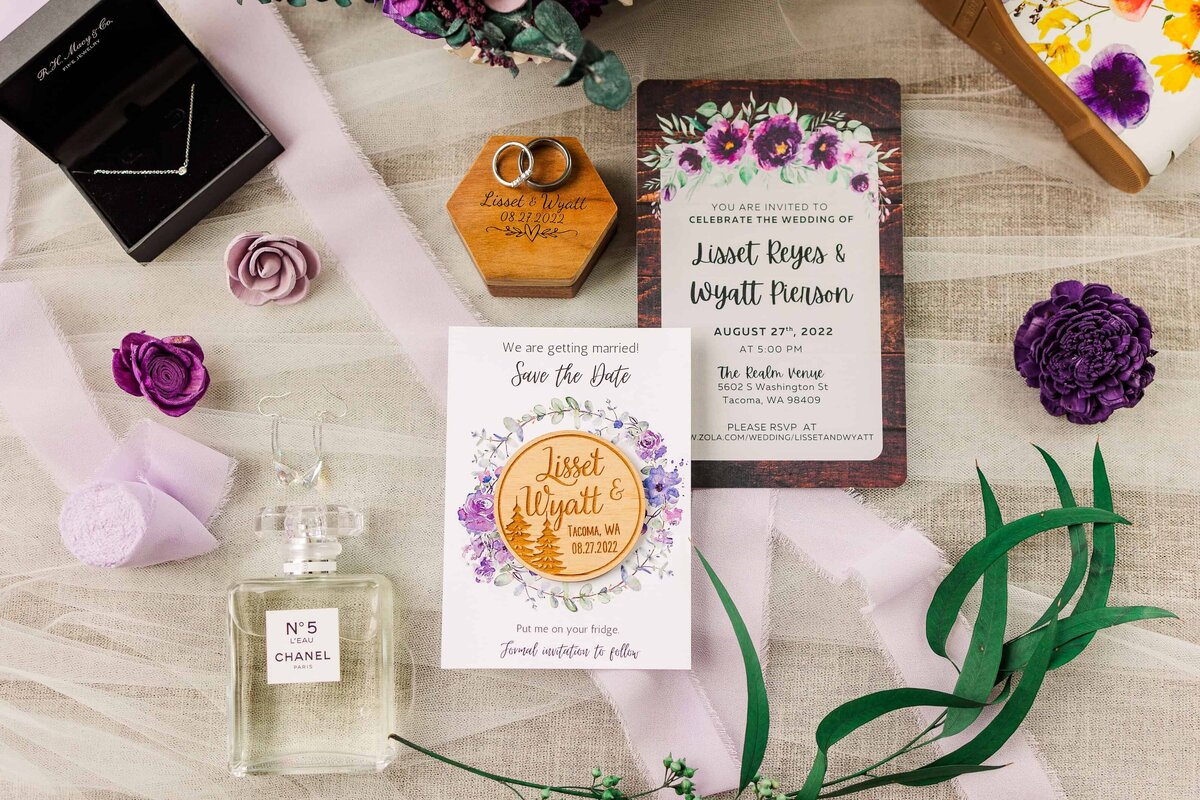 Flat lay photograph of Key wedding, details with purple and green coloring. Details include wedding invitation, save the date, perfume, and rings.