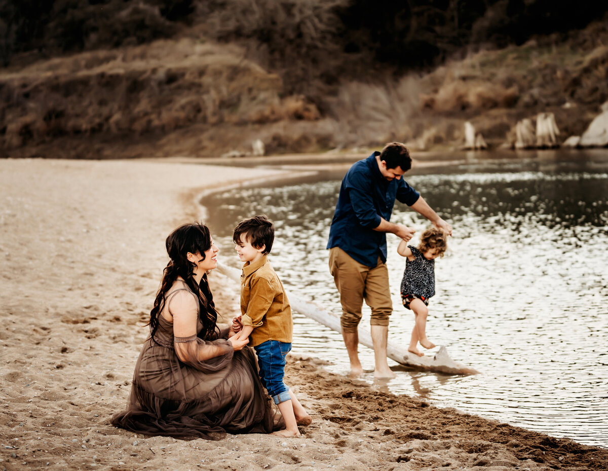 a family of four plays together on the sand of a lake shore