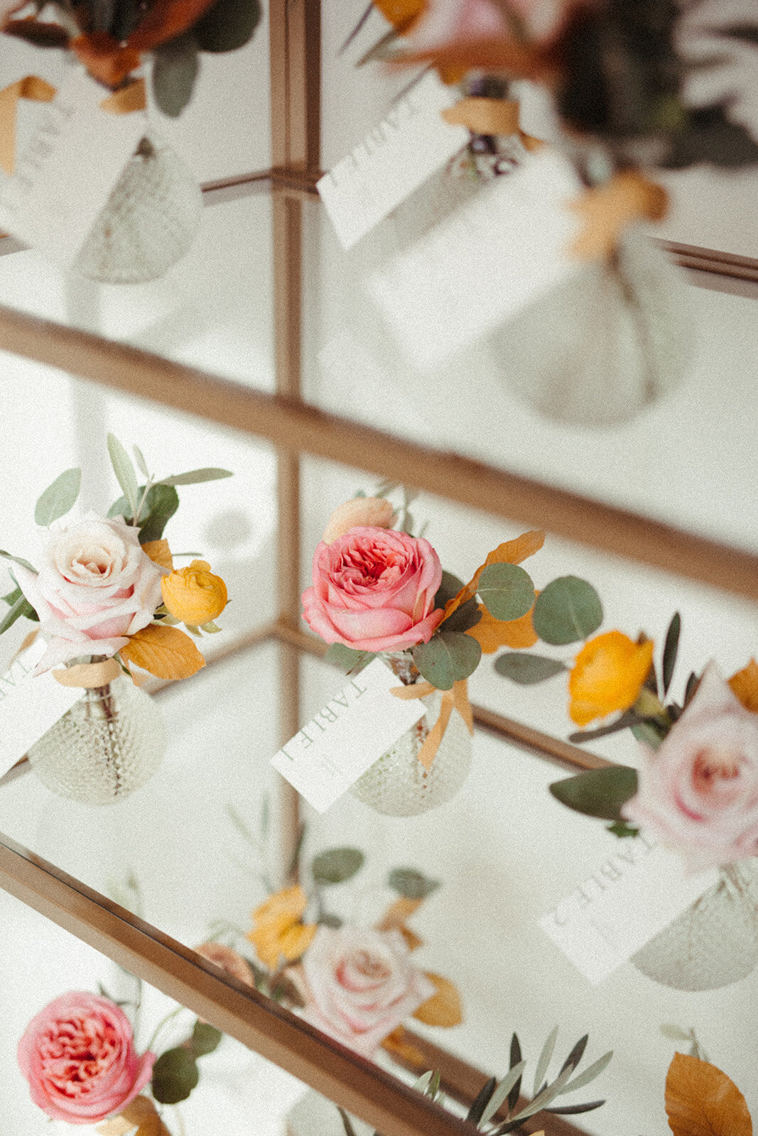 White place cards with light gray font tied to glass vases filled with flowers.