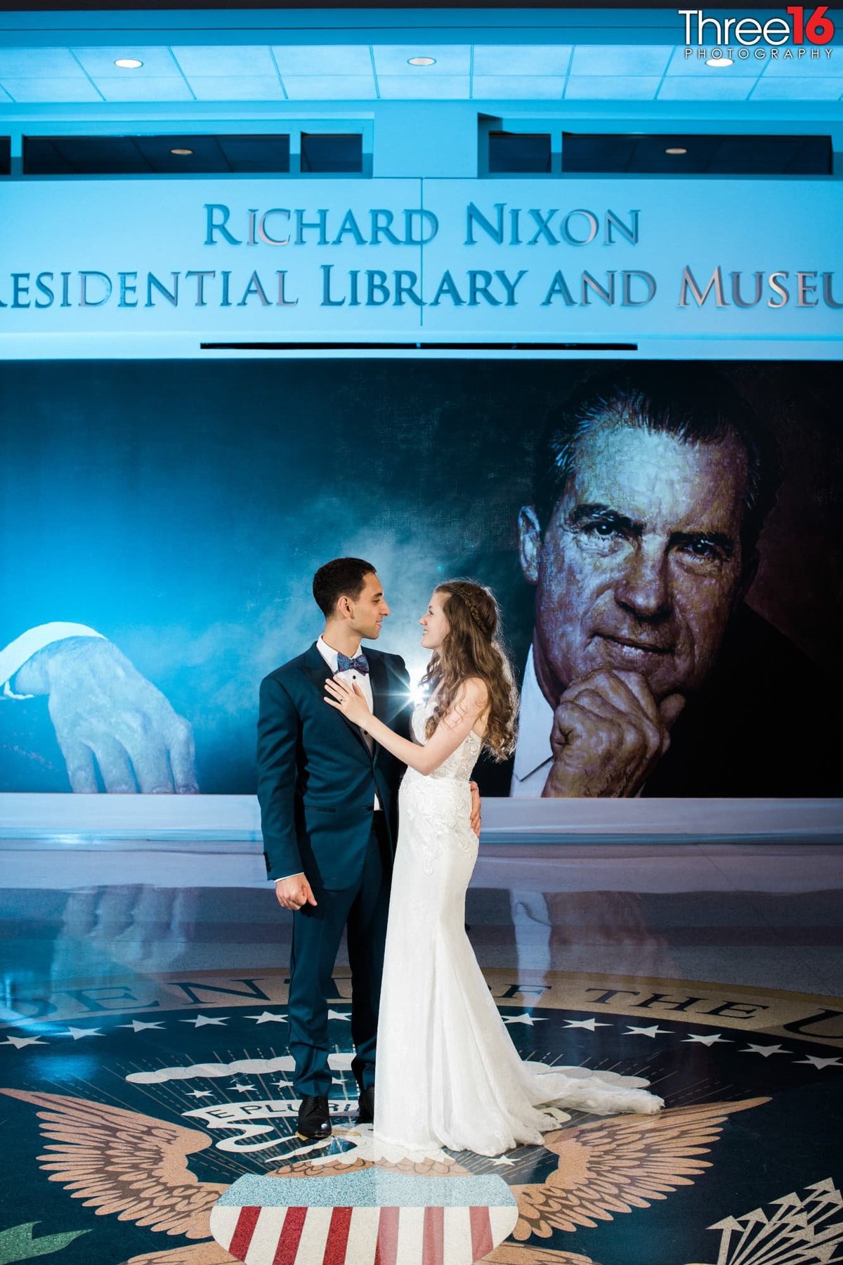 Newly married couple look at each other as they pose in front of the large wall mural of President Richard Nixon
