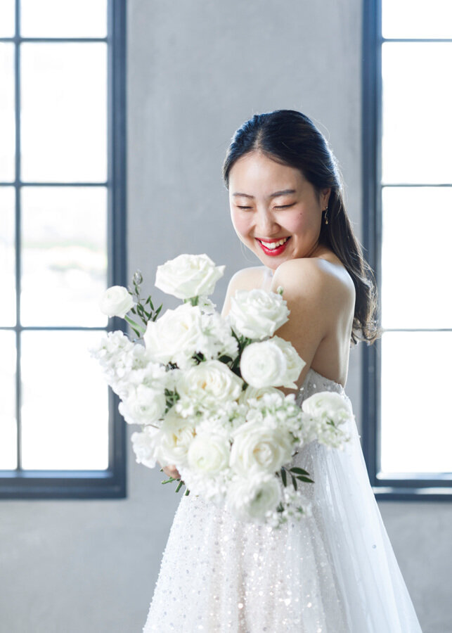Bride smiling down at her white bridal bouquet.