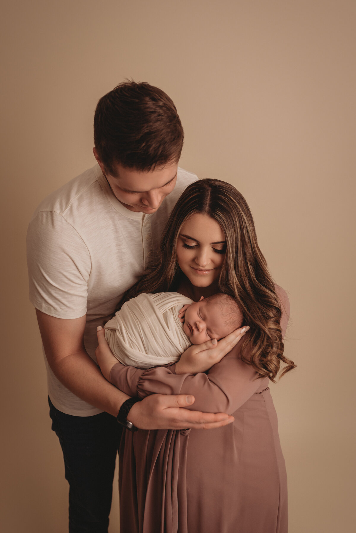 2 week old newborn portrait session with family of three dressed in mauve and creams with mom holding baby while parents look at baby at atlanta family newborn photography studio