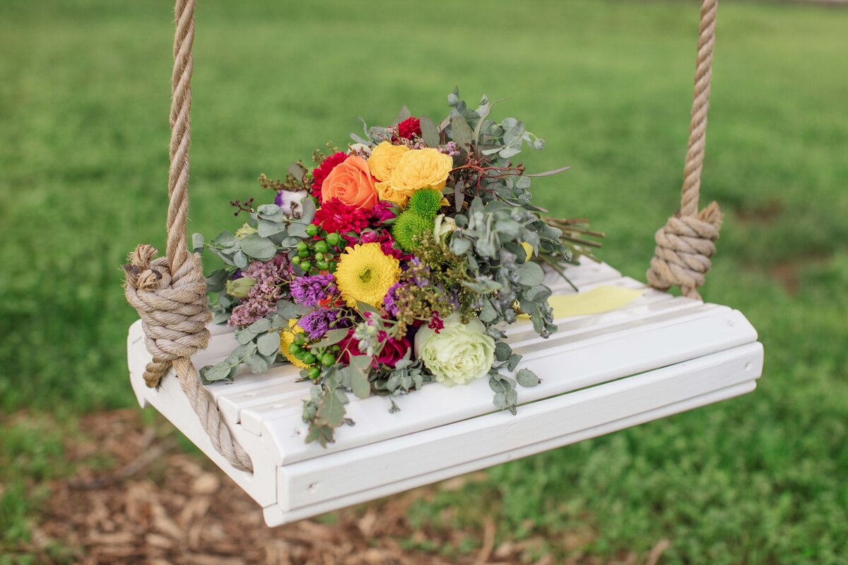 vivid yellow red and orange wedding bouquet sits on wooden swing in San Marcos Texas by Firefly Photography