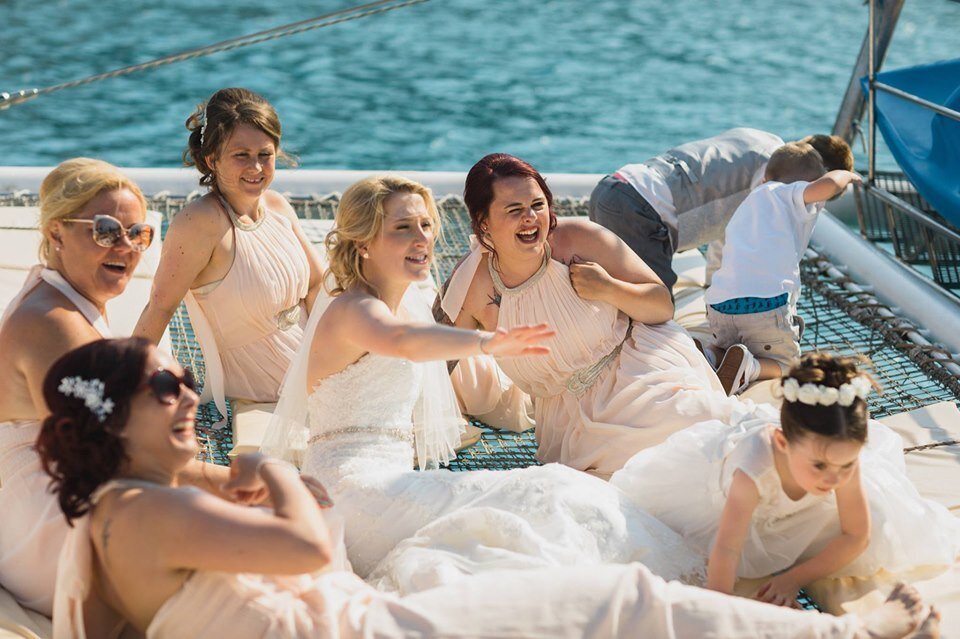 A group of female wedding guests laugh  while cruising the med onboard a catamaran