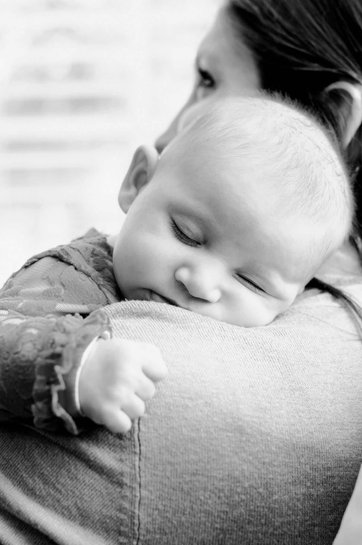 Black and white newborn photography image of a baby asleep on her mom's shoulder, by San Antonio newborn lifestyle photographer Cassey Golden.