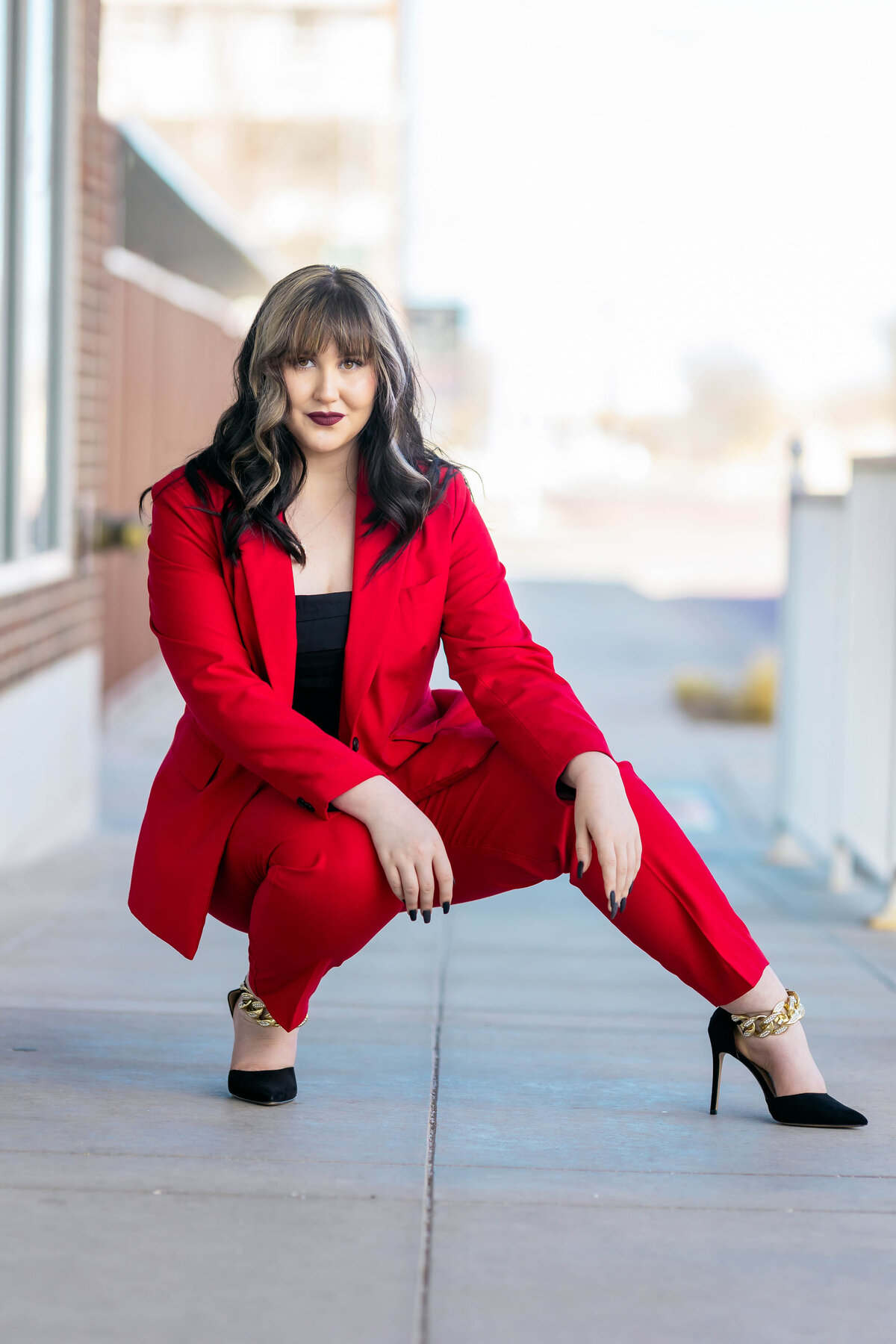 high school senior girl photo session.  girl is wearing a red pantsuit with a black top and black heals looking at the camera