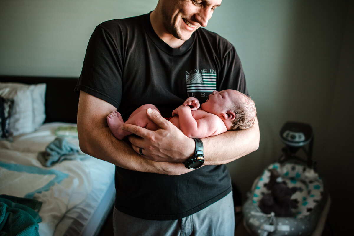 Man smiling and holding a  crying newborn baby