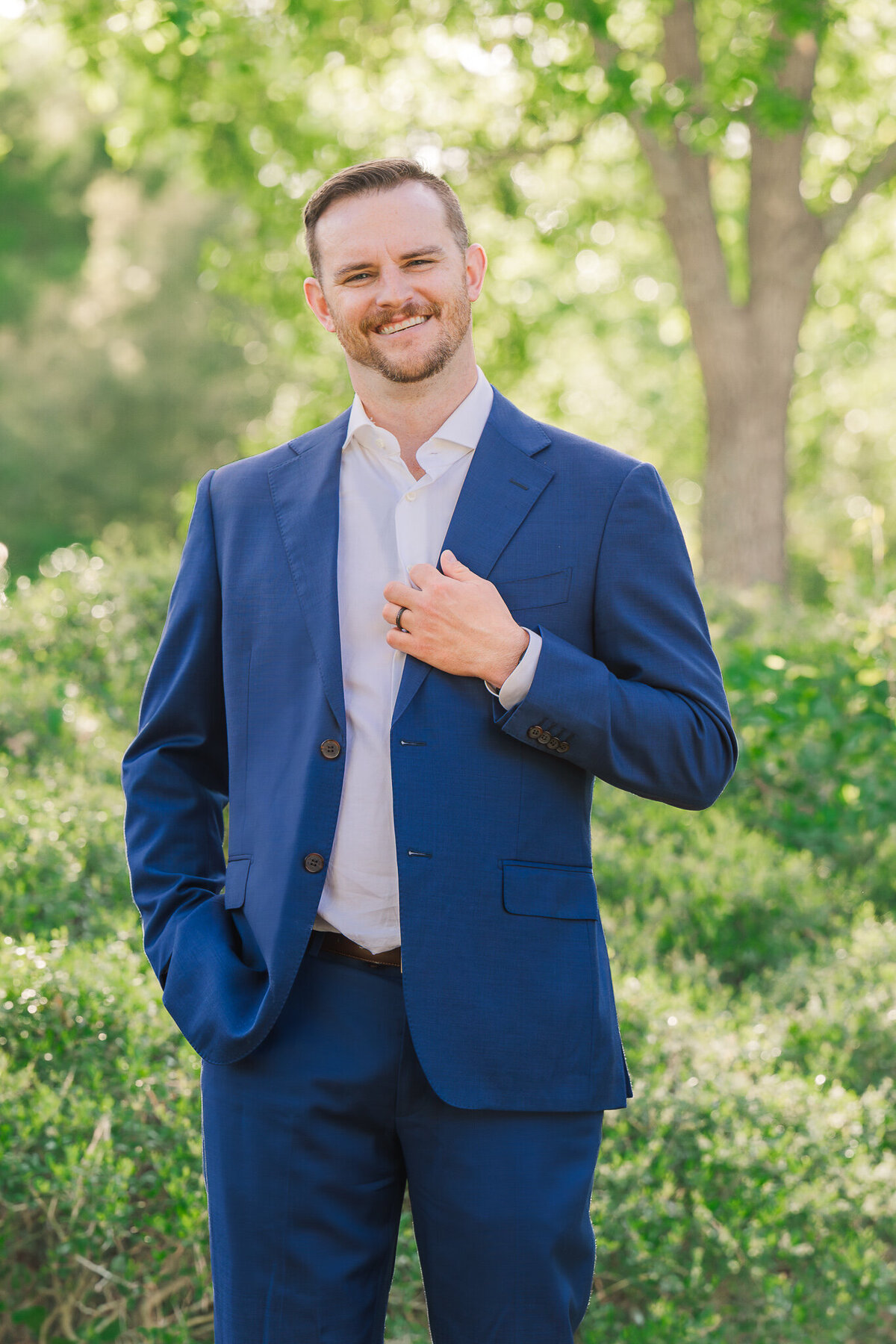 A smiling groom in a blue tux on his wedding day holding his suit jacket enjoying his Wilmington wedding photography session by JoLynn Photography