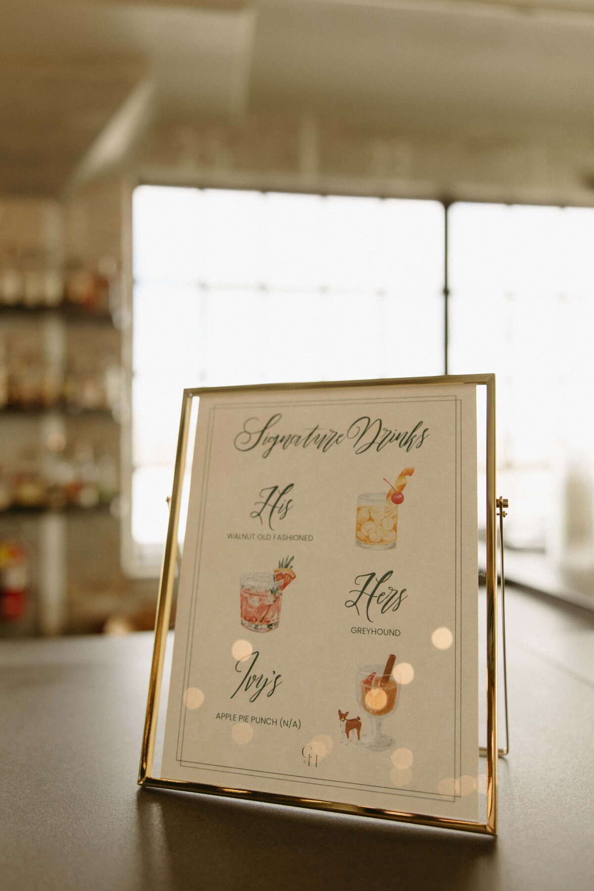 A menu titled "signature drinks" on a stand, displaying cocktail options for Iowa weddings, placed on a table in a softly lit indoor setting.