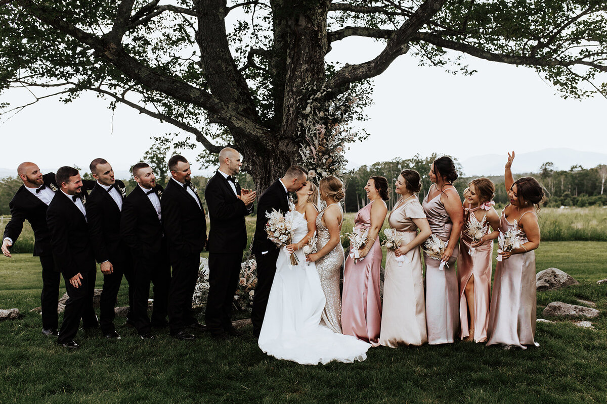 Bride and Groom kissing under the ceremony tree with bridal party looking onward