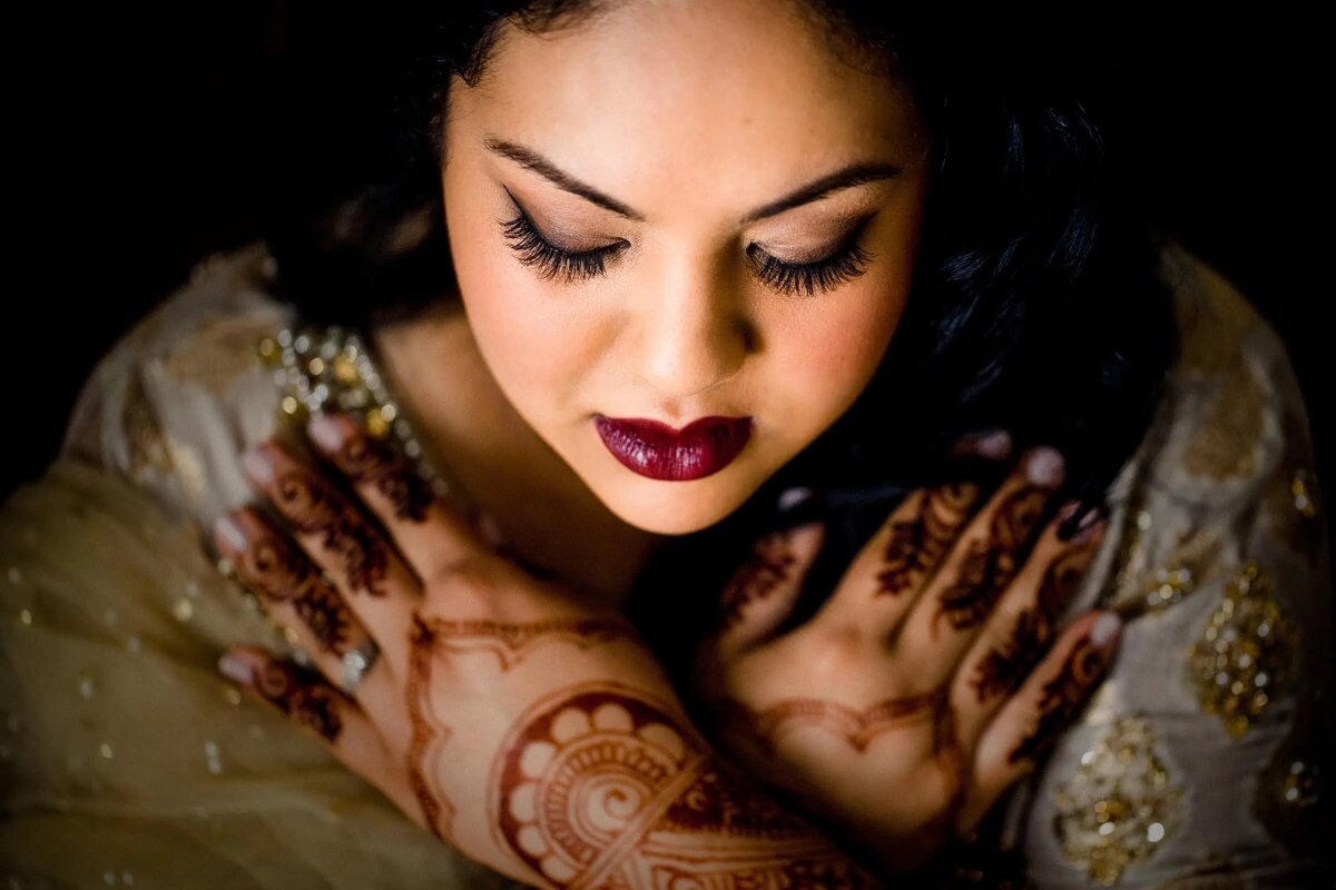 A close-up of a bride, her intricate henna designs complemented by her rich lipstick color