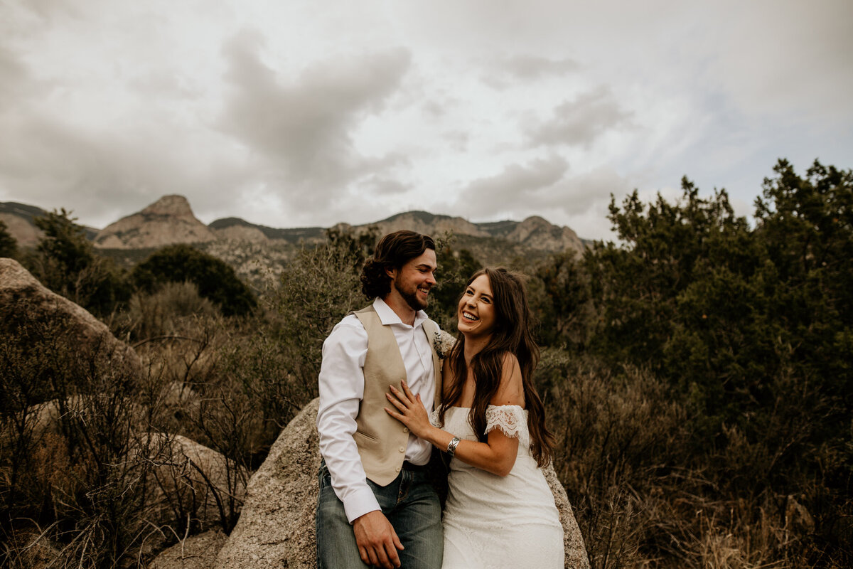 bride and groom sitting against a a rock at the Sandia foothills in Albuquerque