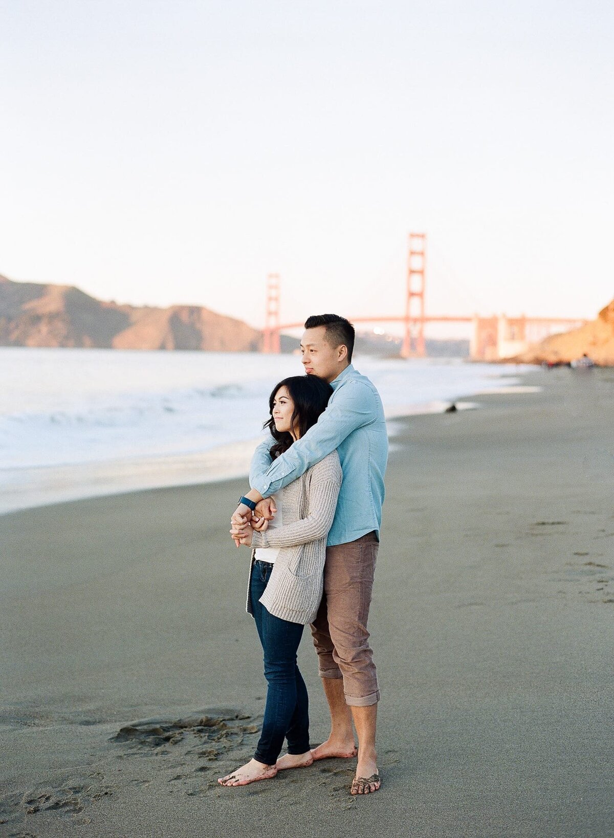 Best laid-back couple portrait photographer in San Francisco. Lady watches the sunset at the beach while her lover hugs her from behind.