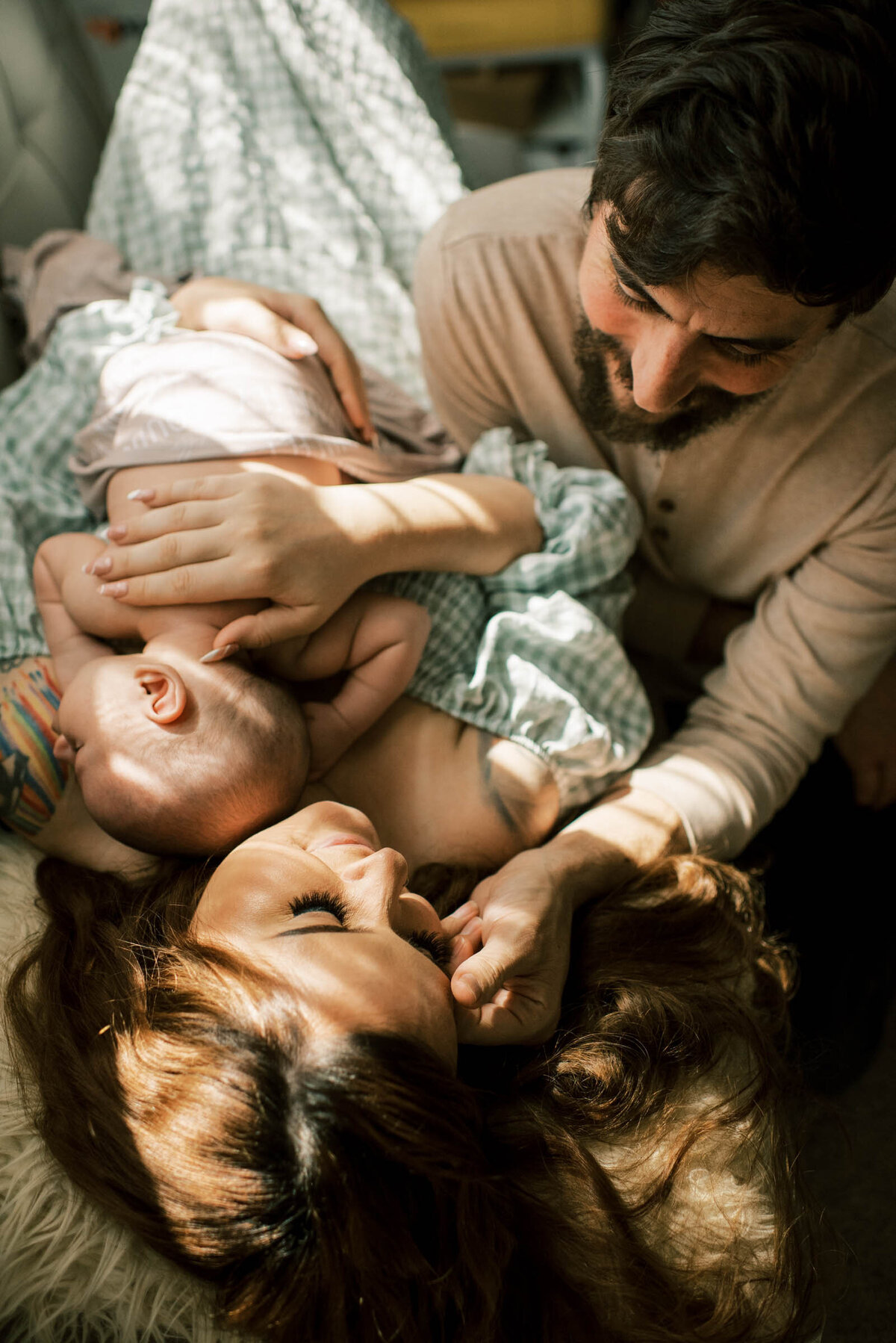 Mother and father lying with newborn baby by the window