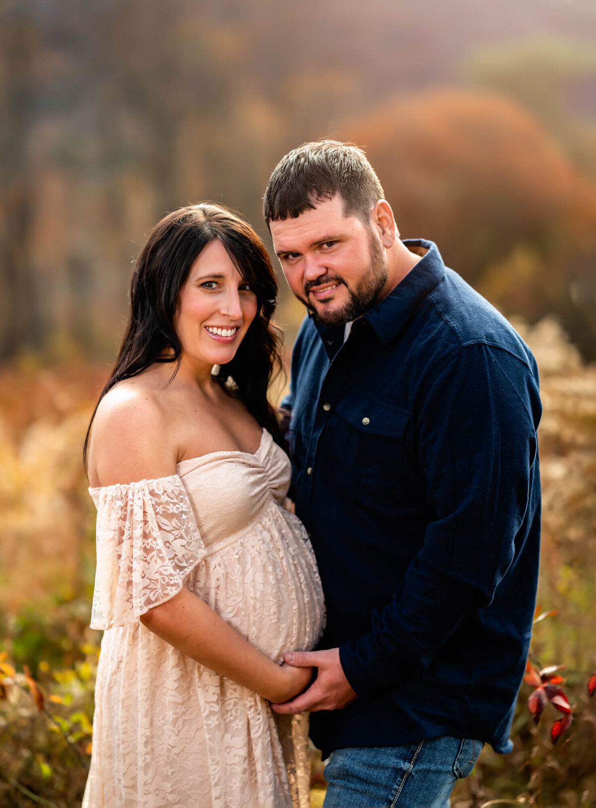 A stunning couple who are expecting parents cradle their bump and smile for the camera during their portrait session with an Asheville Maternity Photographer