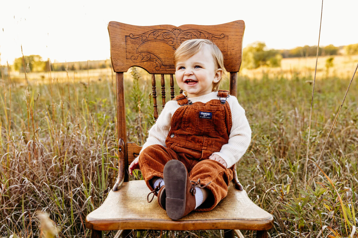 cute toddler boy laughing as his sits on a wooden chair during his milwaukee family photography session