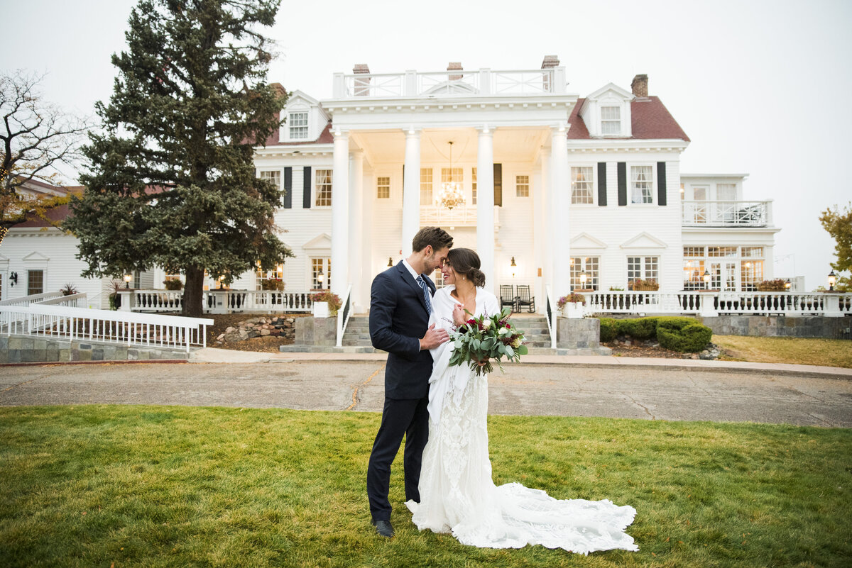 A bride and groom touch foreheads together with The Manor House in the background.