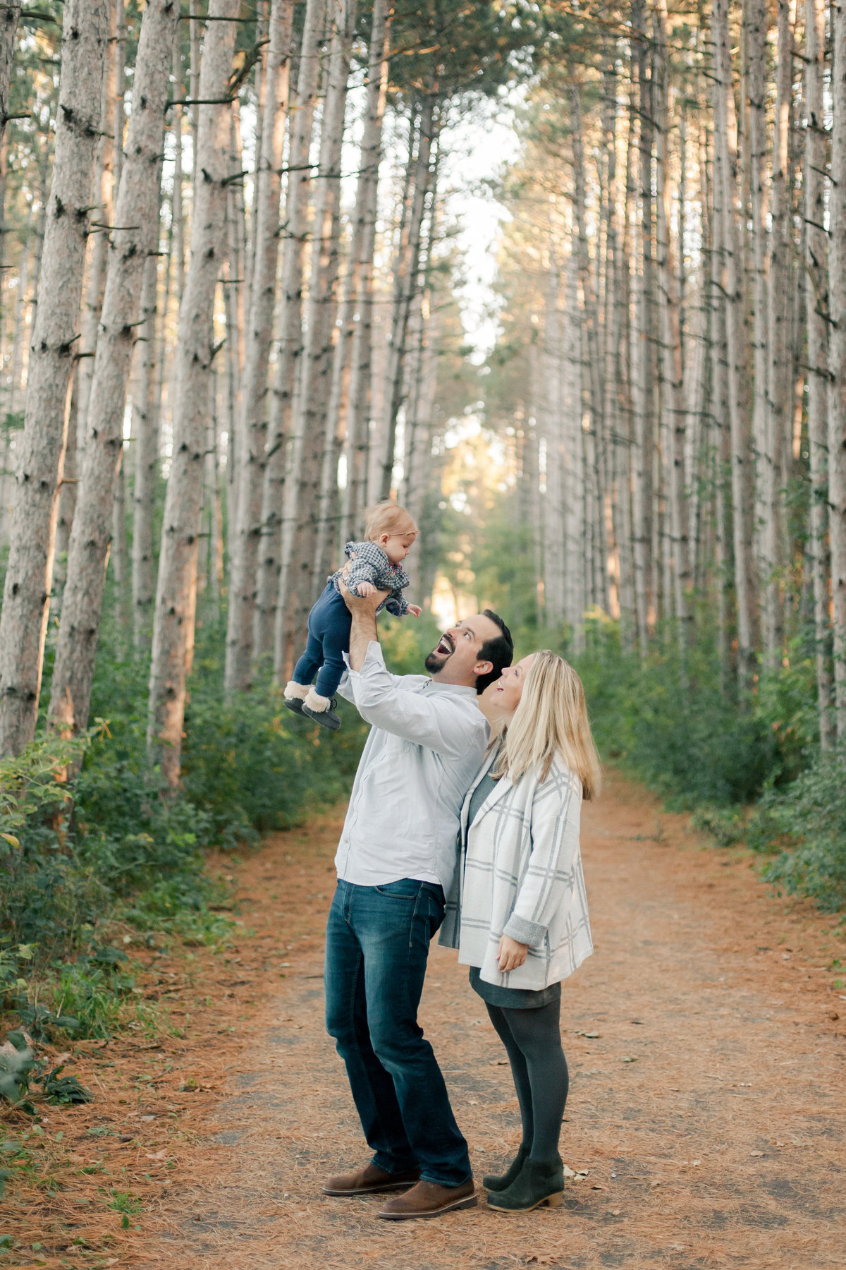 parents of 6 month old baby girl play in the pine forest of twin cities minnesota
