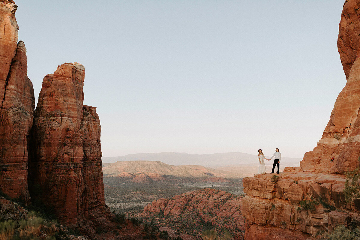 An eloping couple hold hands in Sedona, Arizona atop Cathedral Rock during their elopement 