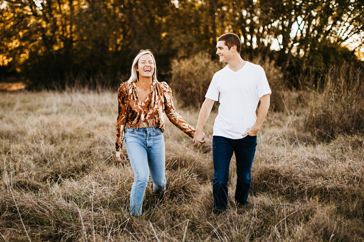 couple holding hands laughing in field at golden hour
