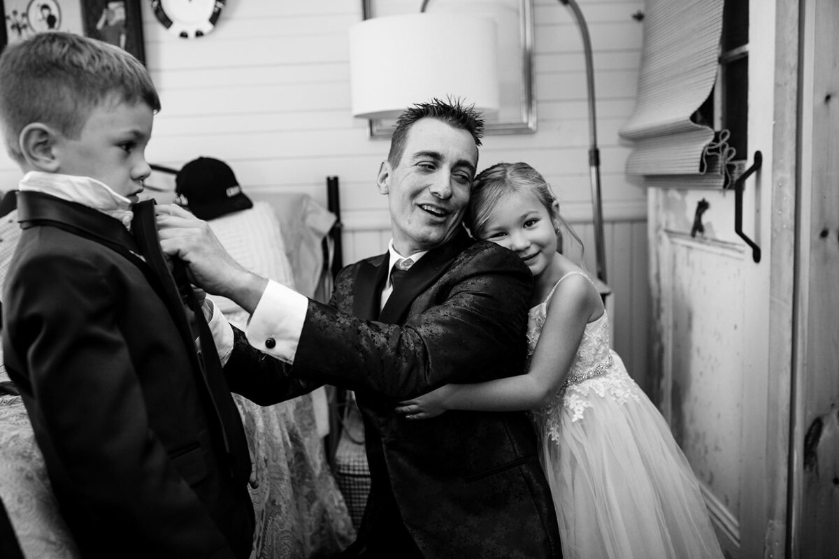 Flower girl hugging groom as he fixes the tie of ring bearer. Getting ready before their first look in North Hatley Quebec