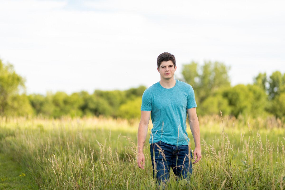 Teenage boy in teal tshirt and jeans walks through field for senior portrait photo