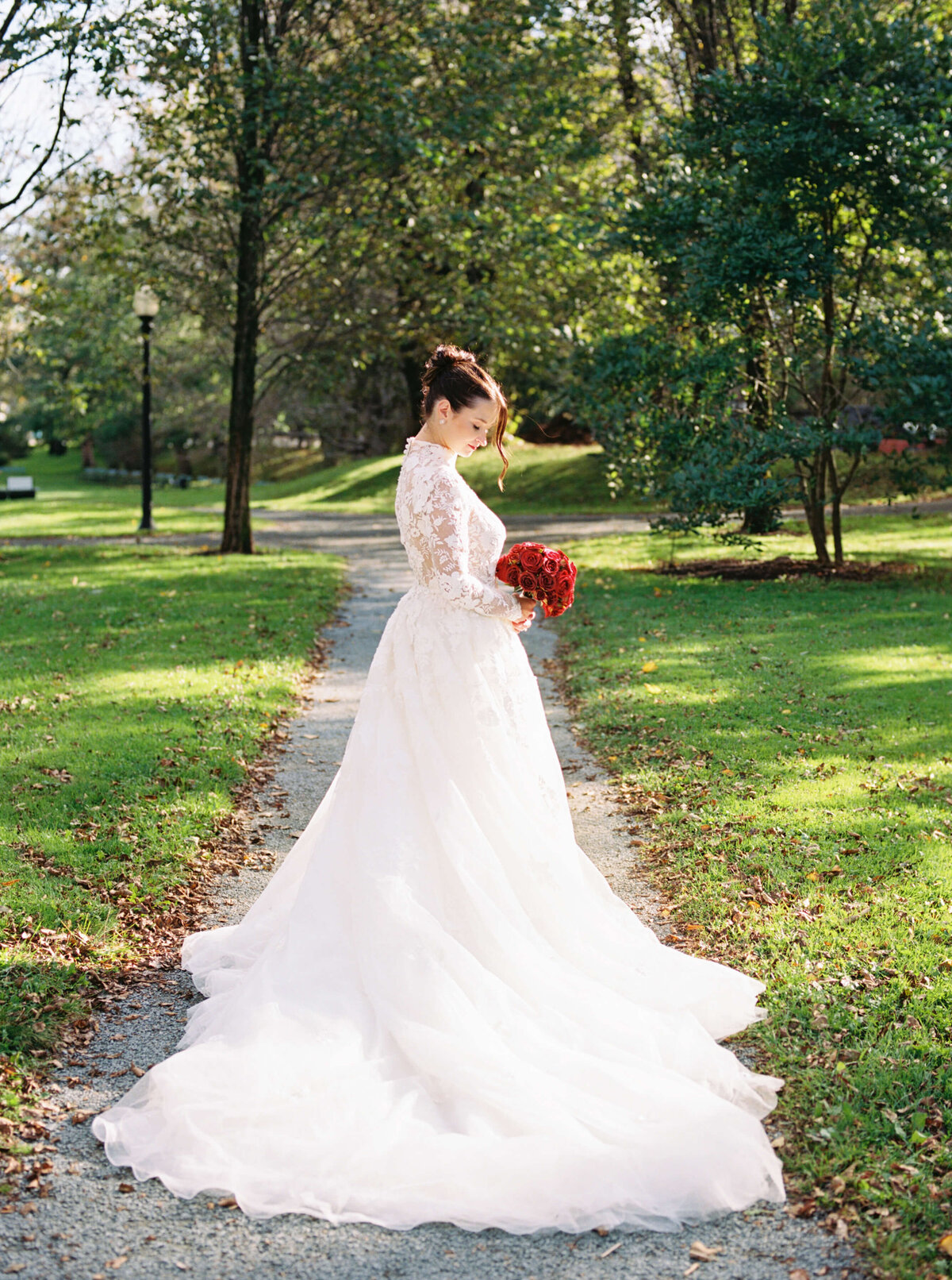 Bride wearing lace dress and carrying red bouquet outside by Halifax wedding photographer, Alyssa Joy Photography