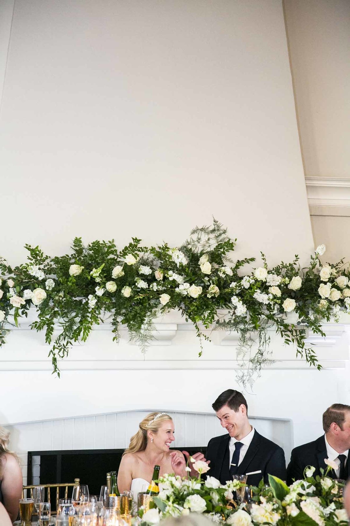 a large wedding arch is framing the bride and groom at their head table, featuring white flowers and greenery