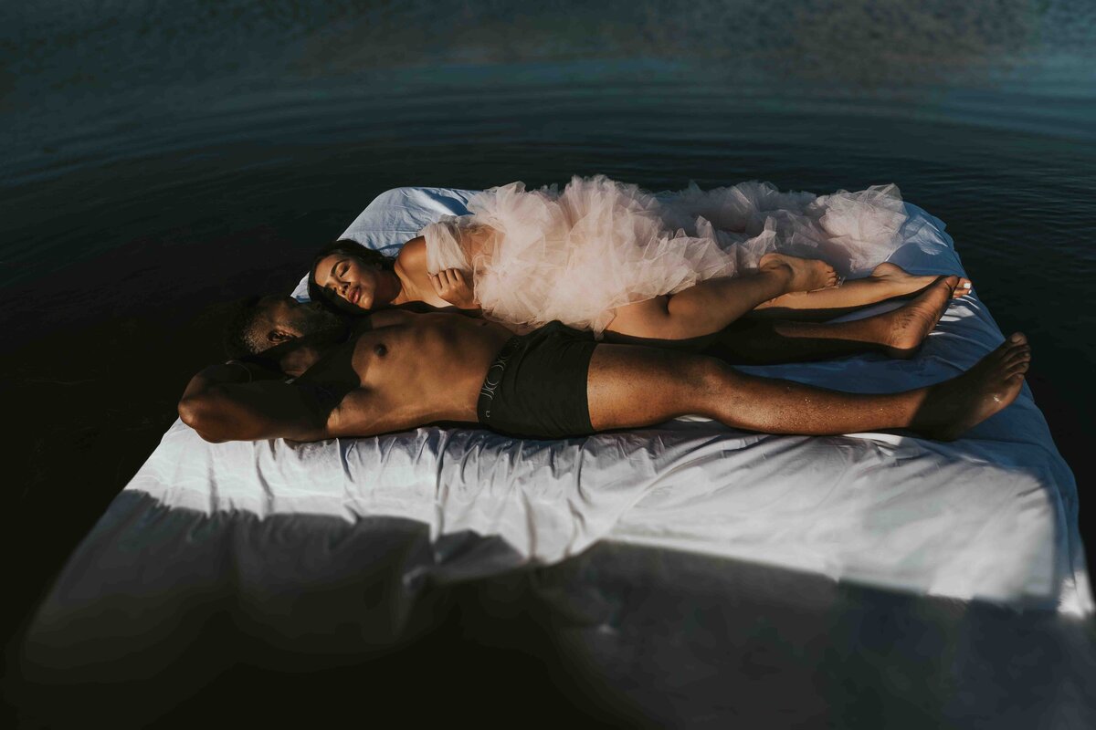 Couple floating on a bed in the middle of a lake only wearing lingerie and boxers