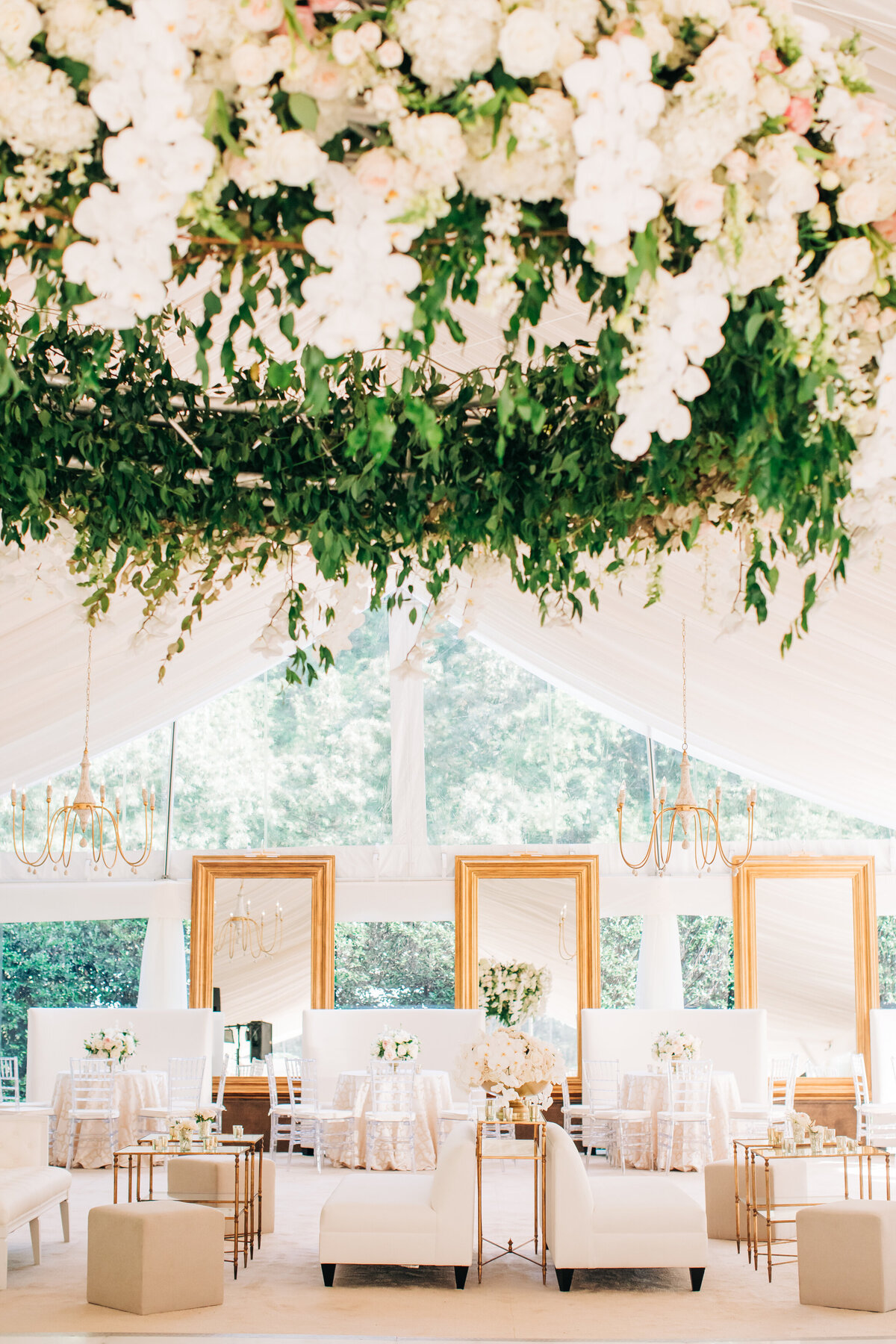 Tented wedding reception with white and gold couches and flowers hanging from the ceiling