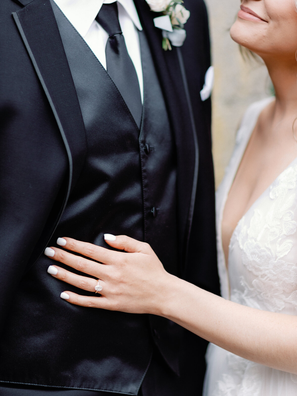 A close up of a bride's hand with her engagement ring placed on top of her groom's chest as she looks up at him