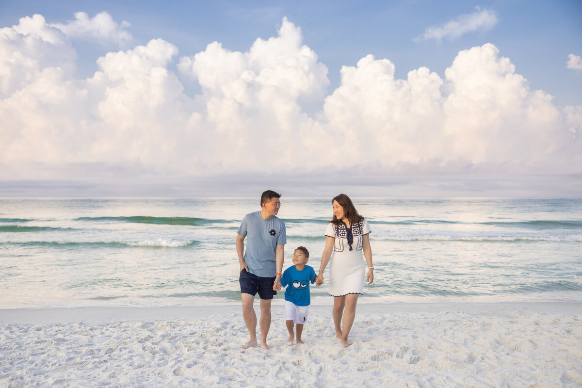 A family of three holding hands and walking along the beach