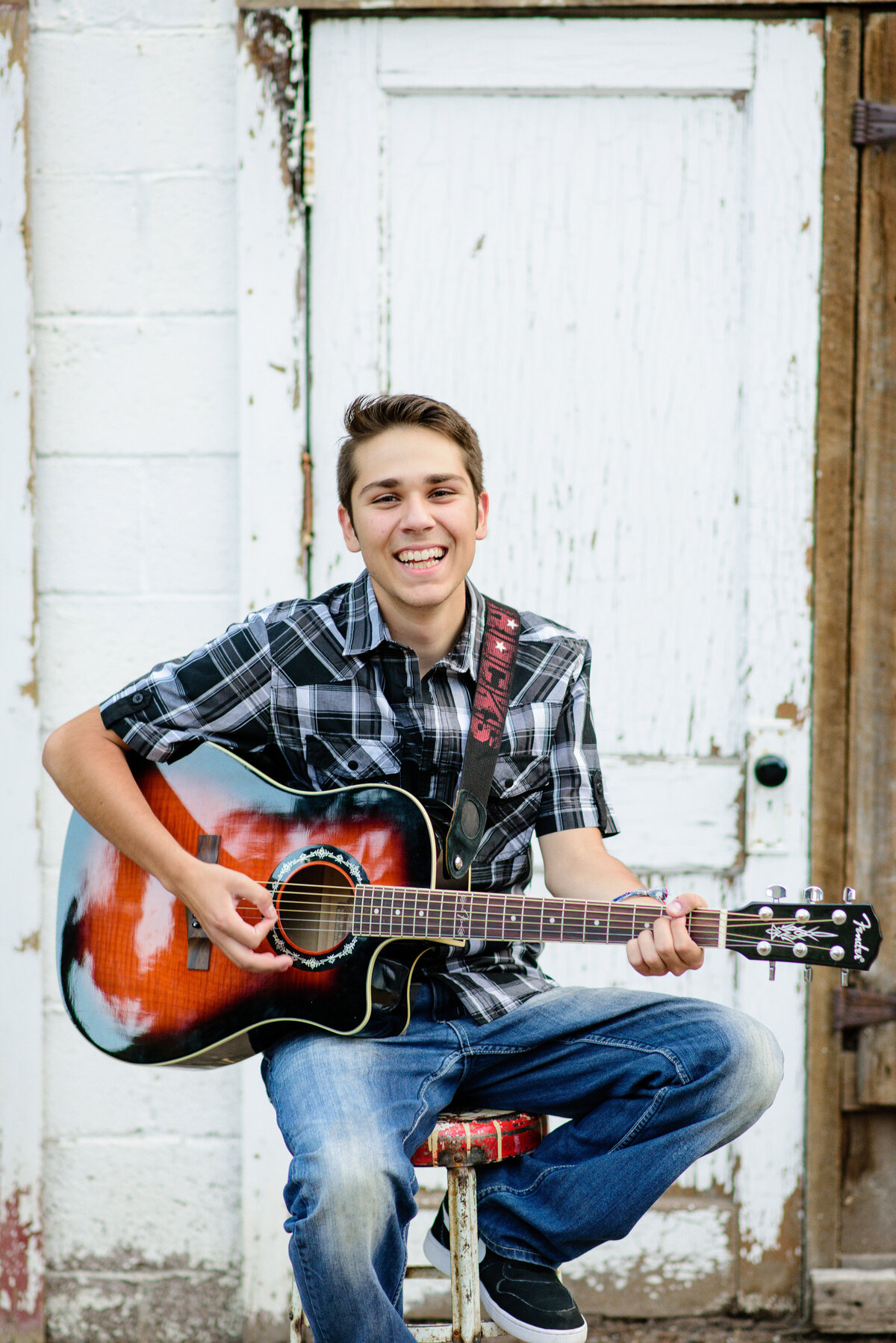 senior photo ideas for guys  with high school senior sitting on a stool with a guitar and smiling as he plays captured by senior picture photographers near me